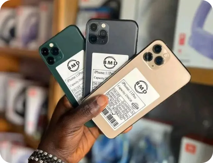 A hand holding three used iPhones with inspection labels